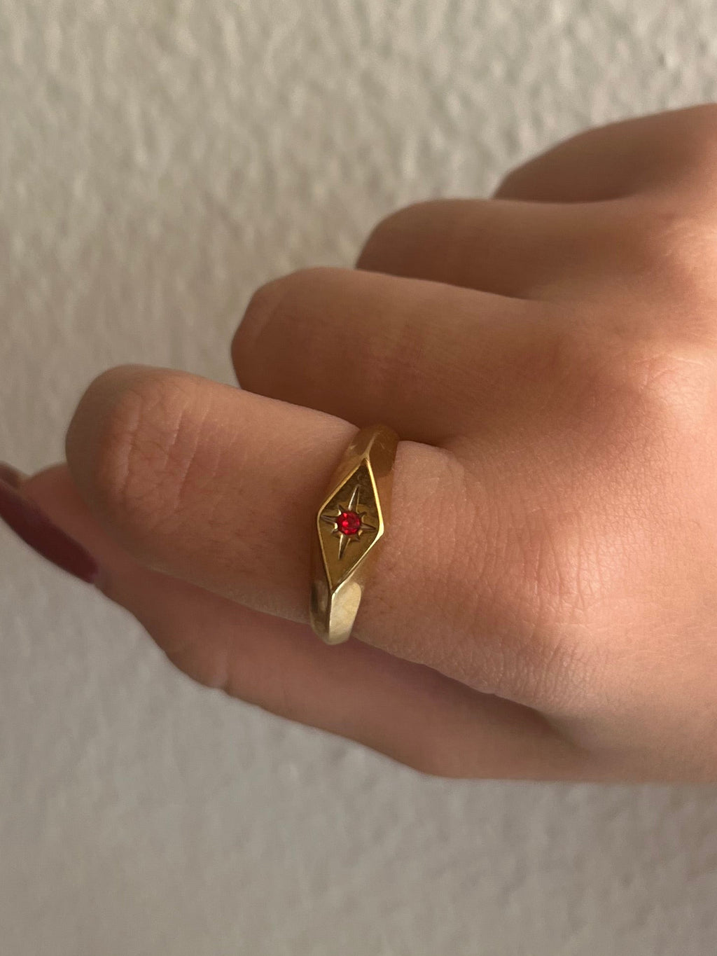 Gold ring with a red gemstone on a person's finger against a plain background